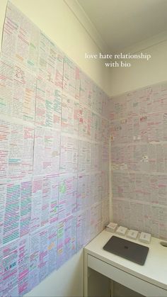 a desk with a laptop on top of it in front of a wall that has many different types of papers written on it