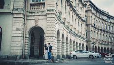 a man and woman standing in front of a building with cars parked on the street