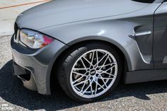 the front end of a gray car with chrome wheels and rims on it's tires