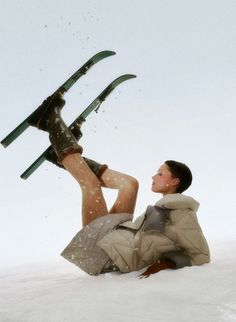 a woman laying in the snow with skis on her feet and legs above her head