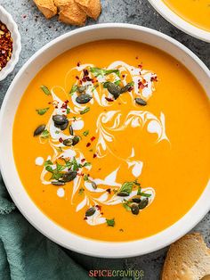 two bowls of carrot soup on a table with bread, crackers and other foods