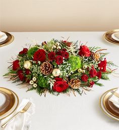 a bouquet of red roses and greenery on a white table cloth with gold place settings