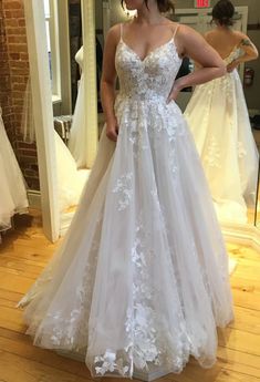 a woman standing in front of a mirror wearing a wedding dress with flowers on it