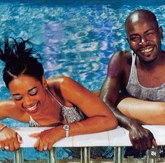 a man and woman sitting next to each other in a swimming pool with their arms on the edge of a railing