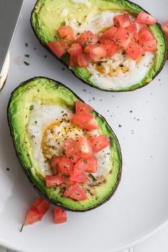 two avocados with tomatoes and eggs on them are sitting on a white plate