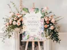 an easel with a welcome sign on it next to flowers and a fire place