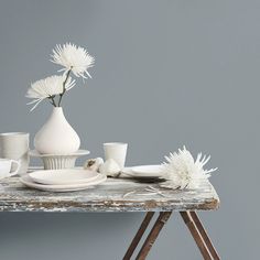 a table topped with white vases and cups filled with flowers on top of a wooden table