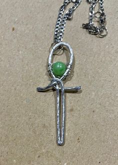 This Ancient Egyptian inspired pendant necklace has been made using aluminium wire, which has been wrapped and hammered to form an Ankh design. The pendant has been decorated with an apple green, glossy, acrylic bead, and is hung on a chunky, 3mm, flat, stainless steel, curb chain, with a lobster claw clasp. Pendant height: 6cm Chain length: 18"(45.5cm) Handmade Metal Ankh Necklace, Handmade Symbolic Green Necklace, Ankh Design, Ankh Pendant, Egyptian Inspired, Art Deco Pendant, Apple Green, Curb Chain, Acrylic Beads