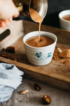 a person pouring something into a bowl on top of a wooden tray next to other bowls