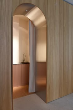 an arched doorway leading to a kitchen and living room area with light wood paneling on the walls