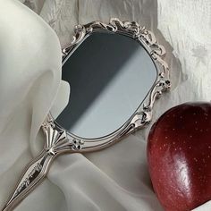 an apple sitting next to a mirror on top of a white cloth covered tablecloth