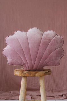 a pink scallop shell sitting on top of a wooden stool