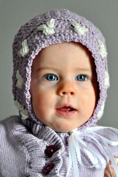 a baby wearing a purple knitted hat with white flowers on it's head