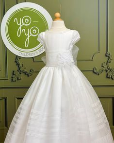 A traditional and classical first communion gown for girls, made with lightweight white organza. It has beautiful pleats throughout the body and skirt. The flower appliqué is removable. It has buttons on the back for closure. Made in Spain Dry clean Does not include crinoline 100% polyester Final Sale Fitted First Communion Dress, Classic Fitted First Communion Dress, First Communion Dress With Ruffles And Fitted Bodice, Classic White First Communion Gown, Classic White Gown For First Communion, Holy Communion Dresses, First Communion Dress, First Communion Dresses, Gowns For Girls