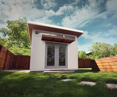 a small white building sitting on top of a lush green field next to a wooden fence