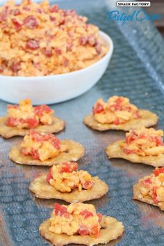 crackers with cheese and tomato toppings are on a baking sheet next to a bowl of dip