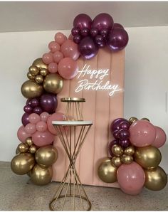 a pink and gold balloon arch with happy birthday written on it next to a table