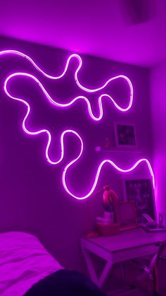 a purple room with neon lights and a white desk in front of the wall is a bed