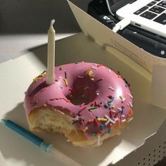 a pink donut with a candle in it sitting on top of a desk next to a laptop