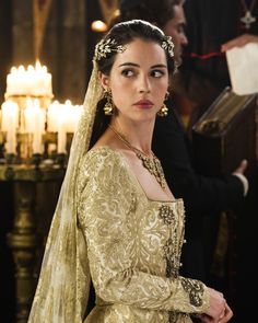 a woman wearing a gold dress and headpiece in a room with candles on the walls