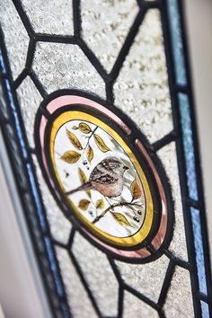 a stained glass window with a small bird on it's side and leaves in the center