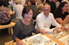 two people sitting at a table with wine glasses in front of them, smiling for the camera