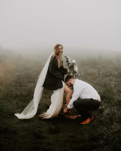 a man kneeling down next to a woman in a wedding dress on top of a grass covered field