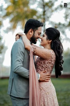 a man and woman embracing each other in front of trees