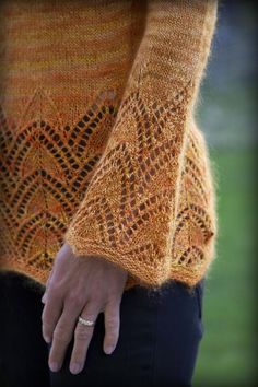 a close up of a person's hand wearing an orange knitted sweater and black pants