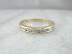 a gold wedding band with five diamonds on it, sitting on a white marble surface