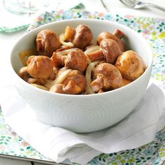 a white bowl filled with meat and onions on top of a floral table cloth next to utensils