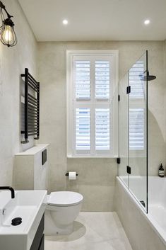 a white toilet sitting next to a bath tub under a window