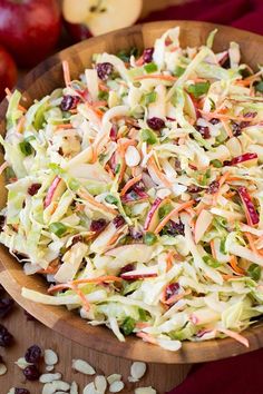 a wooden bowl filled with coleslaw slaw next to apples and raisins