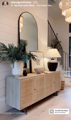 a large white vase sitting on top of a wooden dresser next to a mirror and lamp