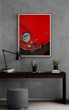 a red car is hanging on the wall above a desk with a lamp and potted plant