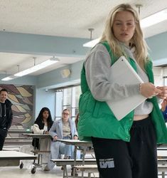 a woman in a green vest holding a binder while standing next to other people