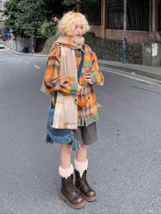 a woman standing on the side of a road wearing boots and a plaid coat over her shoulders