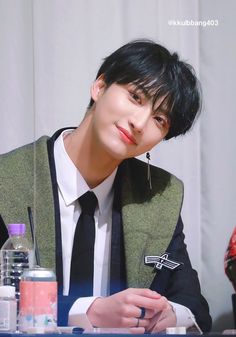 a young man sitting at a table in front of a bottle of water and wearing a tie