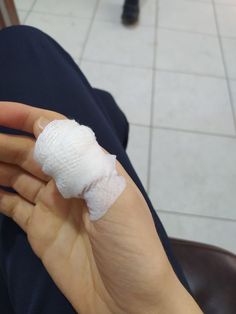 a hand with a bandage on it holding something in their left hand while sitting next to a tile floor