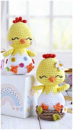 two crocheted chickens sitting next to each other on a white table with a window in the background