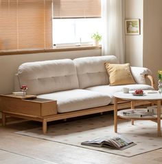 a living room with a white couch and coffee table in front of a window that has blinds on it