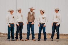 a group of men standing next to each other in front of a white building wearing cowboy hats