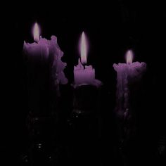 three lit candles sitting in the dark with one glowing purple and one pink on each candle