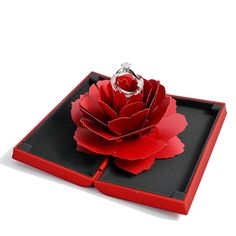 a ring sits on top of a red flower in a black box that is open