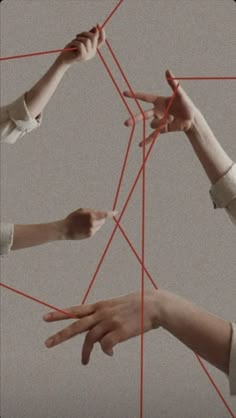 four hands reaching up to the center of a string structure with their fingers pointing towards each other