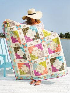 a woman holding up a colorful quilt on top of a wooden deck next to water