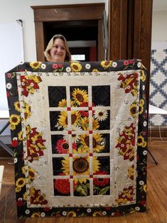 a woman holding up a quilt with sunflowers on it