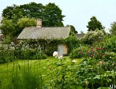 an old cottage surrounded by lush green grass and flowers in the foreground is a garden with pink roses