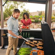 a man and woman grilling vegetables on an outdoor grill with food in the background