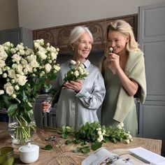 two women standing next to each other in front of a table with flowers on it